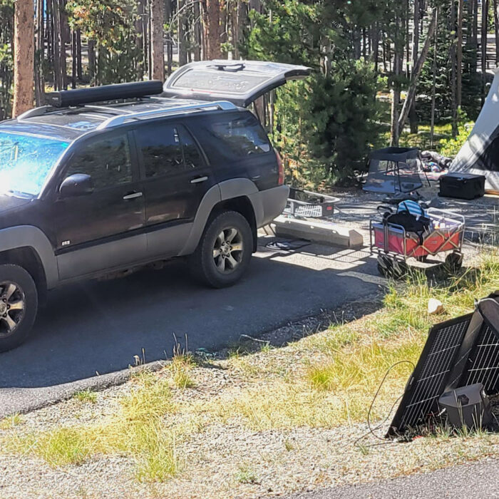 a campsite with a car unloading gear such as a tent, solar panel, wagon, and more for our review of the best car camping gear.