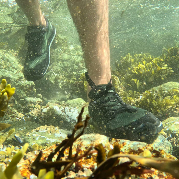 a man walks across a rocky ocean bottom in water shoes
