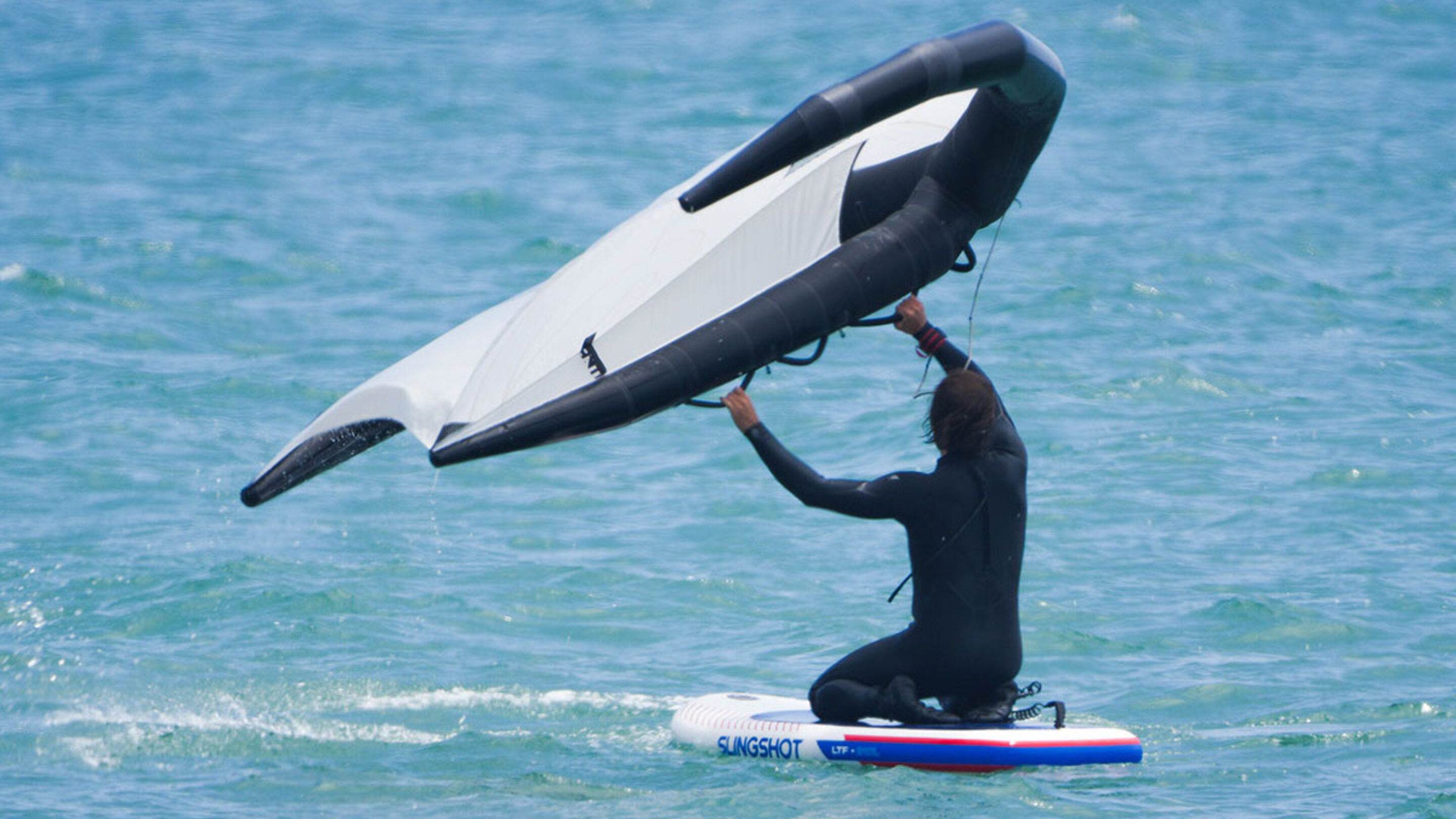 a man learning how to wing foil by starting on his knees on the slingshot ltf board in the water.