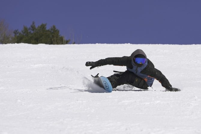 a snowboarder carving up a large heelside bottom turn on a nidecker snowboard