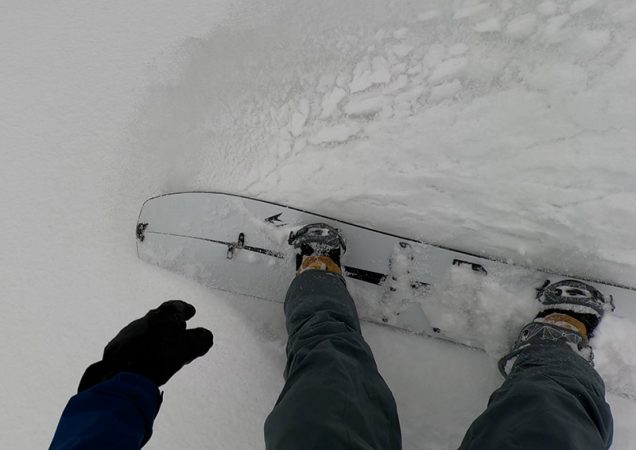 a look down at a snowboard kicking up a spray of snow on the jones mind expander splitboard