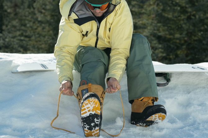 a snowboarder laces up his snowboard boots while reviewing the top picks