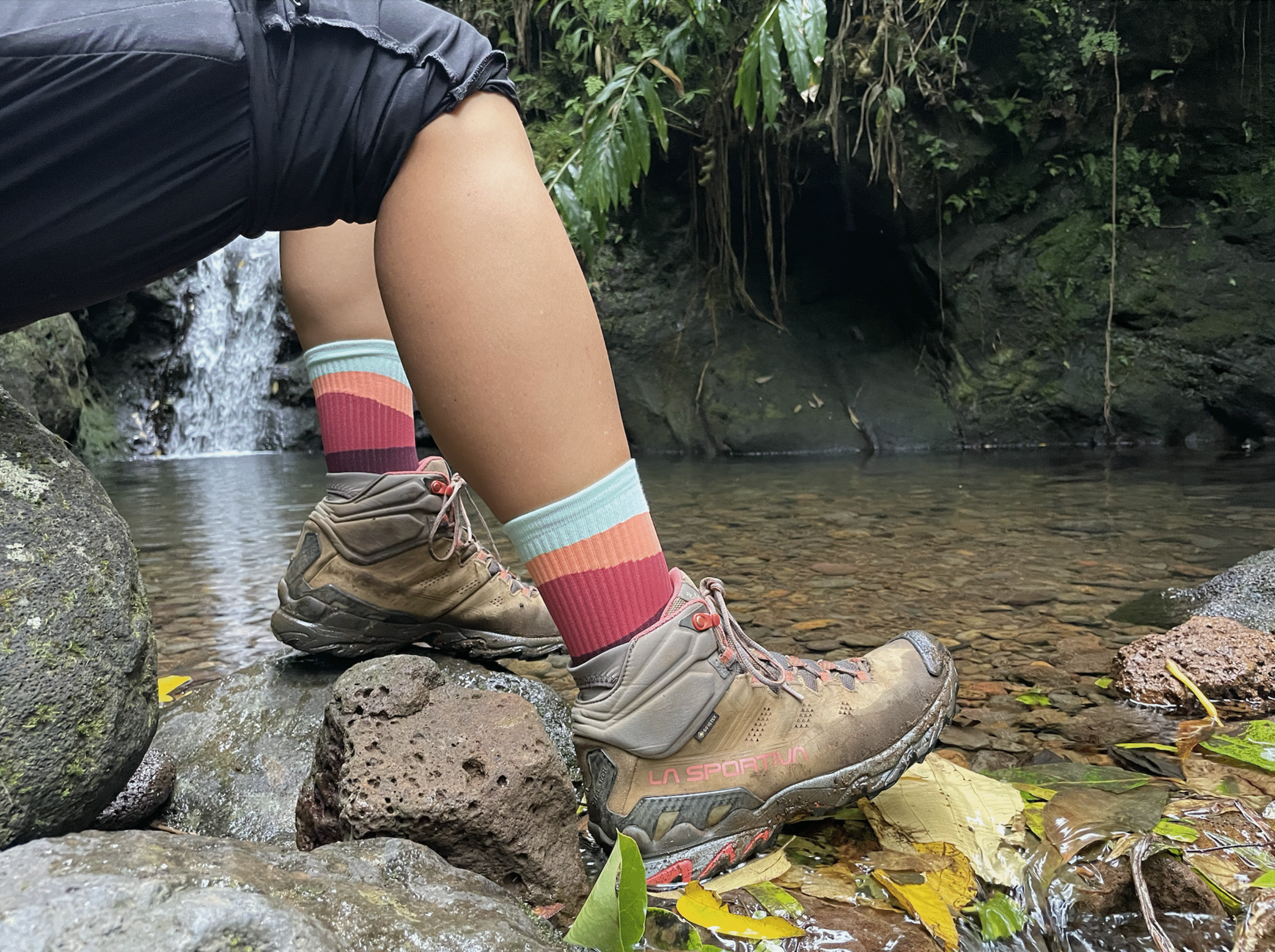 two feet with socks and boots on the edge of a pond