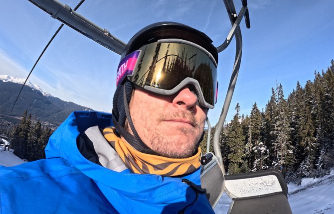 a snowboarder on a chairlift wearing the smith squad imprint ski and snowboard goggles