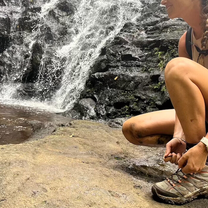 a woman ties her shoes next to a waterfall