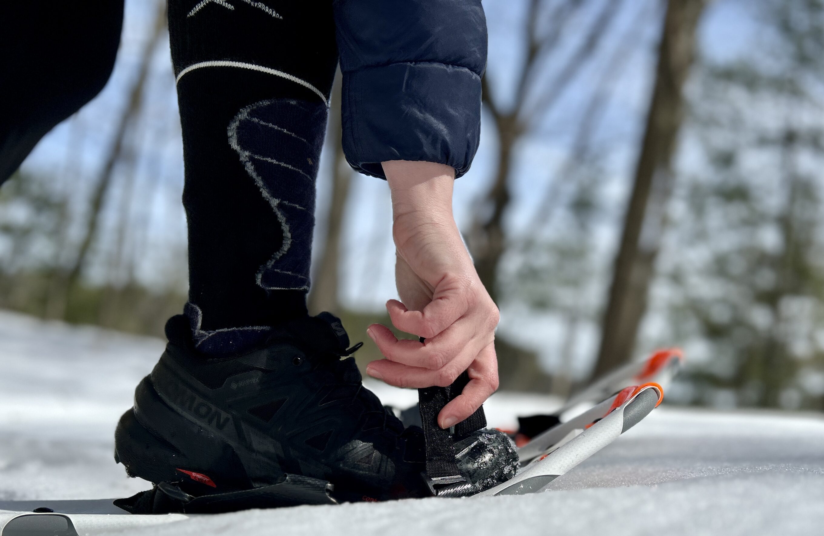 A woman adjusts the bindings on the Dion 121 snowshoes 