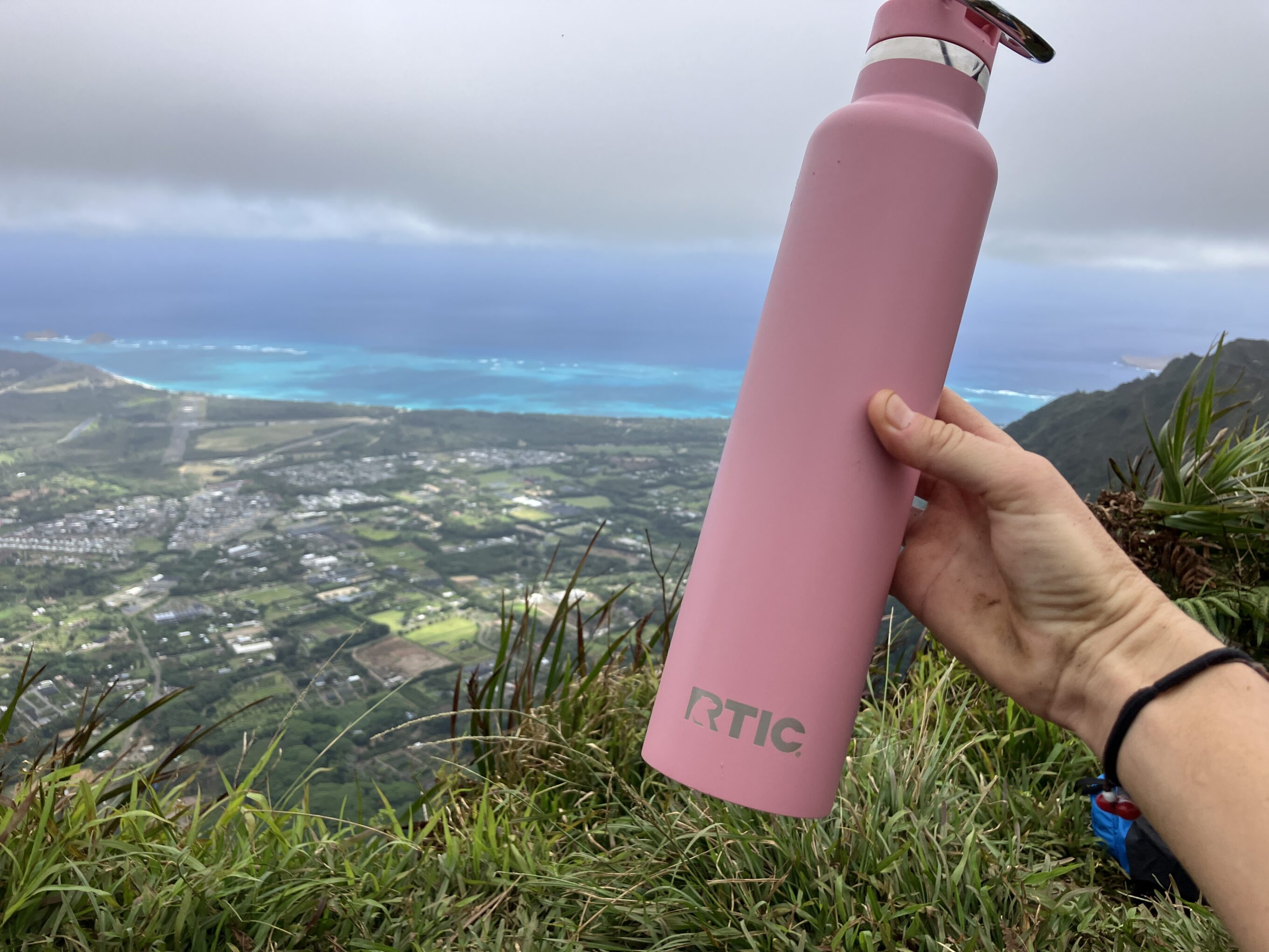a water bottle held over a view from a hiking trail