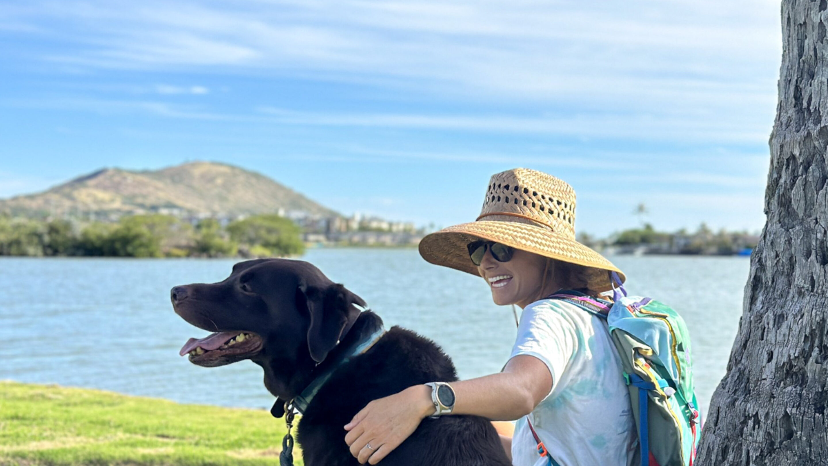woman in a sun hat sitting by the water with a dog