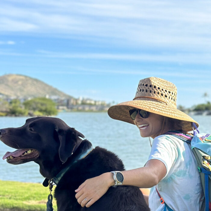 woman in a sun hat sitting by the water with a dog