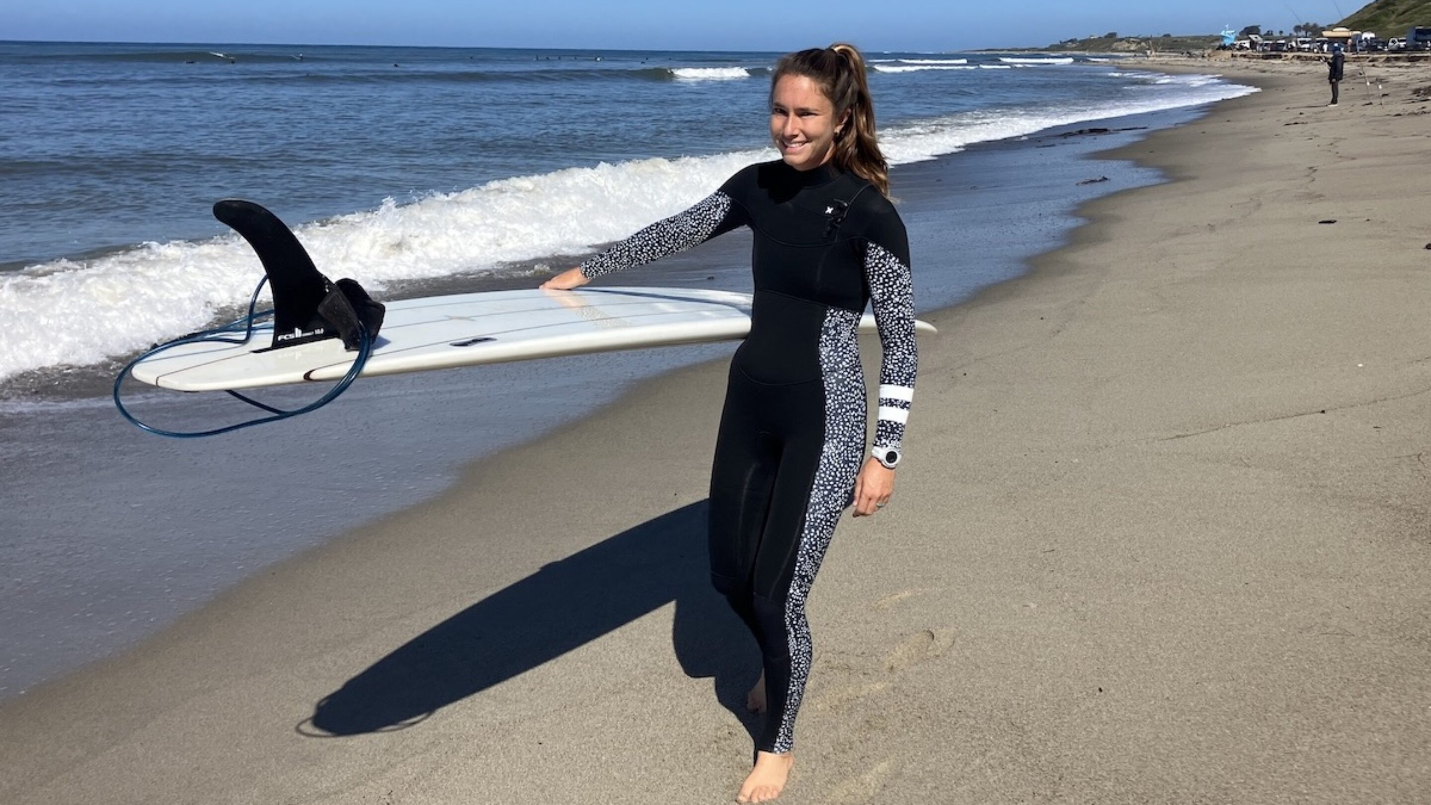 a woman wearing a hurley wetsuit walking on the beach with a surfboard