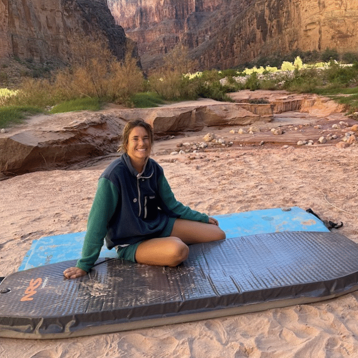 a woman wearing a fleece jacket sitting on a sleeping pad