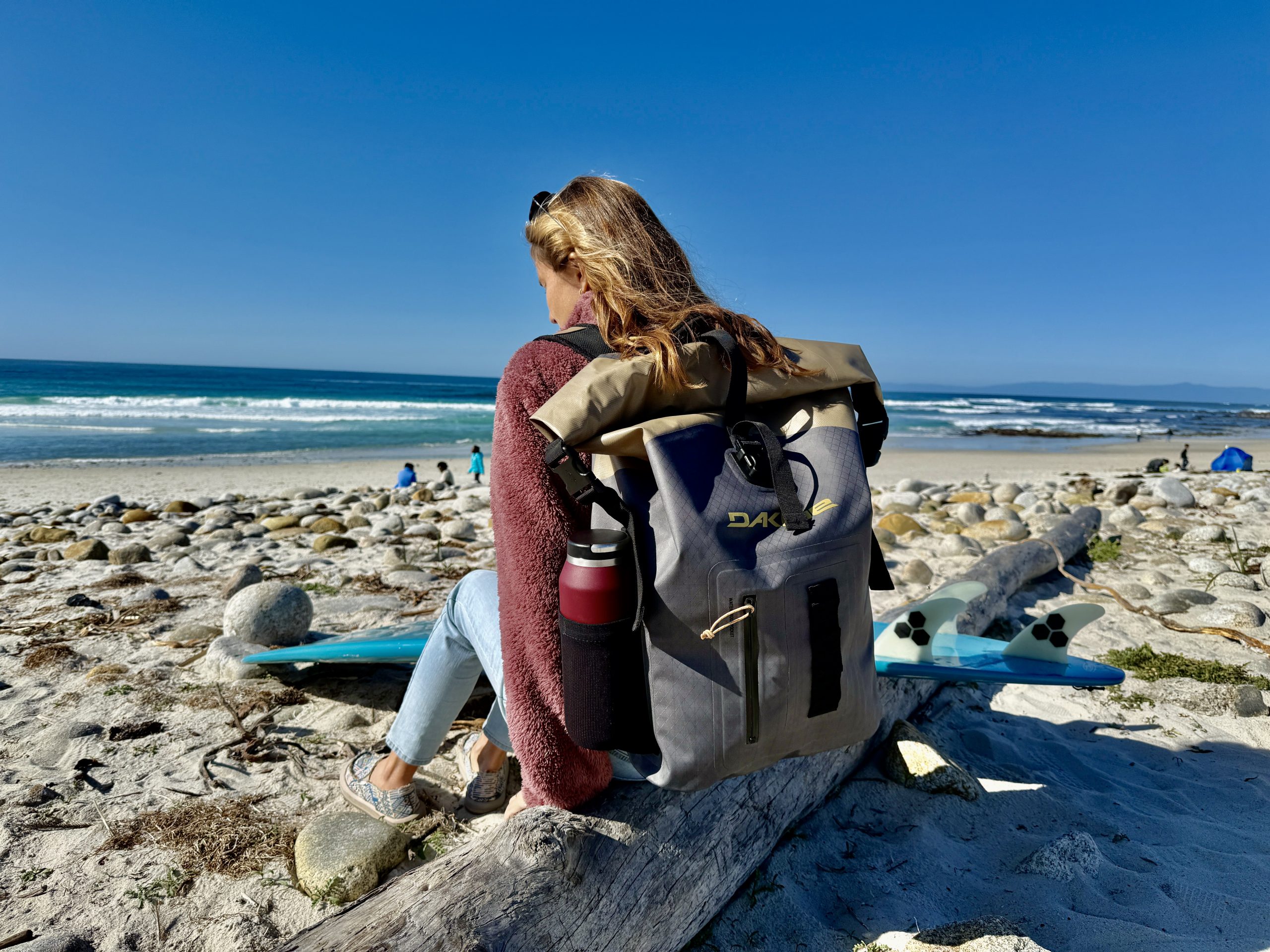 a woman wearing a dakine cyclone surf backpack at the beach