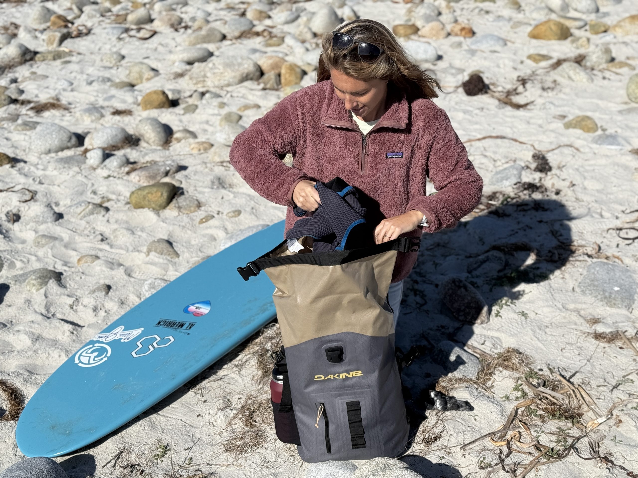 a woman pulling a wetsuit out of a surf backpack