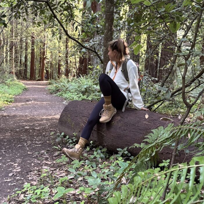 a woman sitting on a log wearing hoka kaha hiking boots