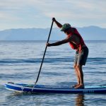 A man paddling an inflatable paddle board at dusk on Lake Tahoe