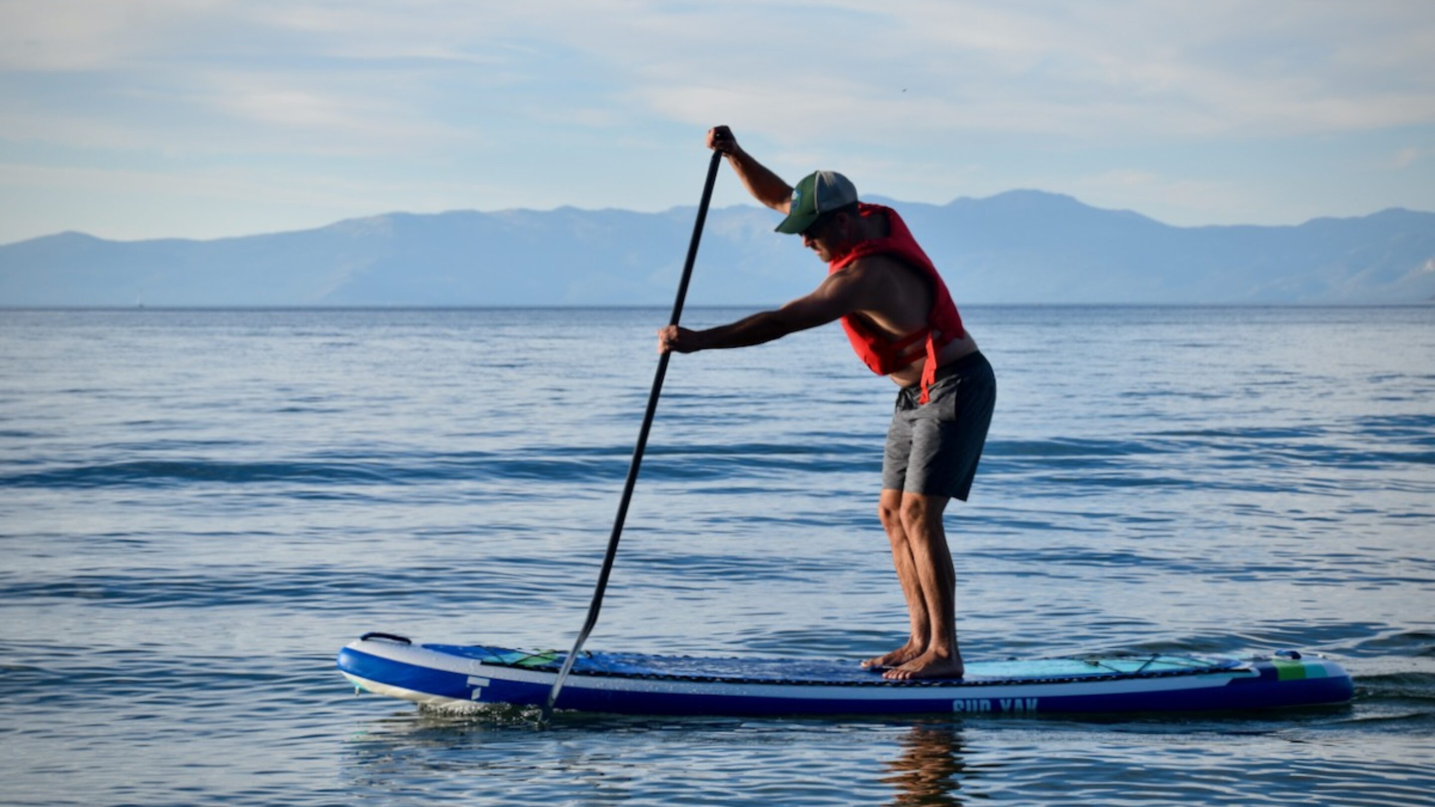 A man paddling an inflatable paddle board at dusk on Lake Tahoe