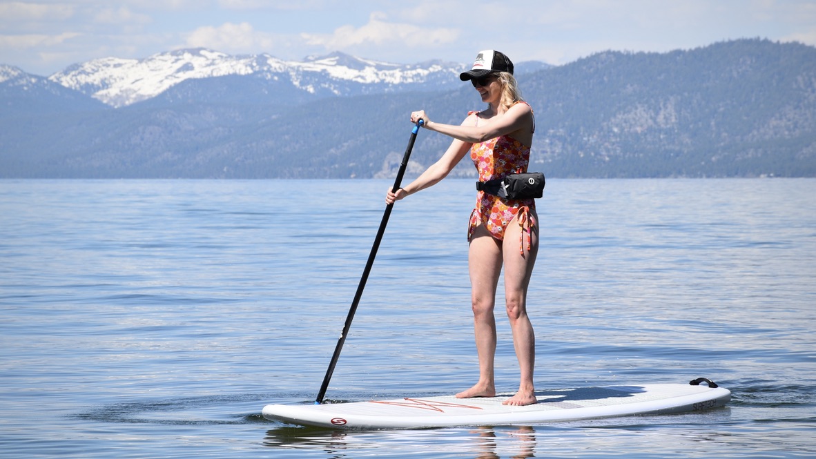 beautiful woman paddle boarding on lake tahoe with mustang survival essentialist life jacket