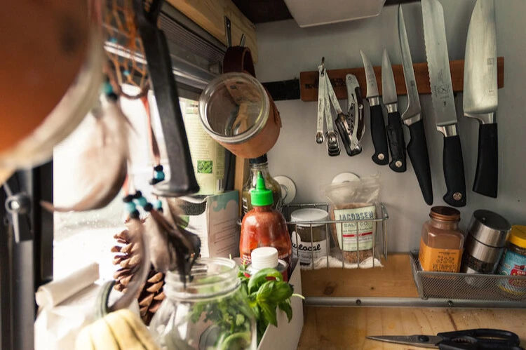 A closeup photo of a camper van kitchen using magnetic wall storage for knives and measuring spoons