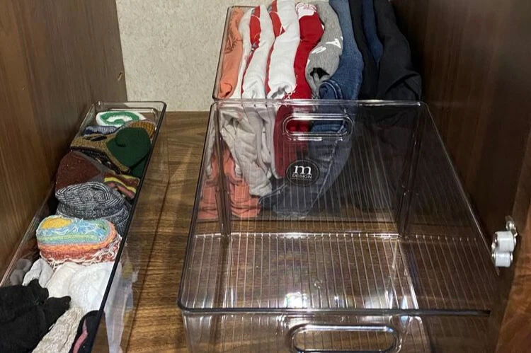 A closeup photo of clothes stored in clear storage bins in a closet