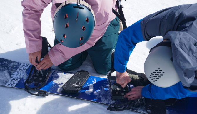 Adjusting bindings on a snowboard wearing the Anon Merak with adjustable vents