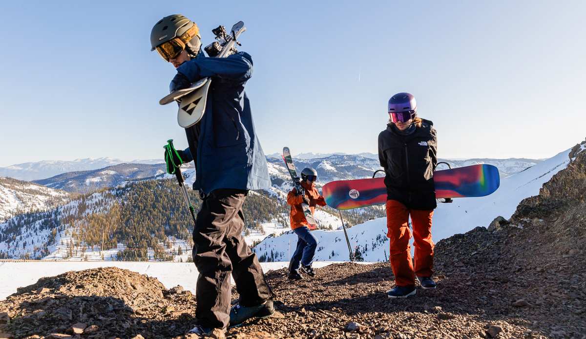 three men hiking up mountain with snowboard and ski gear