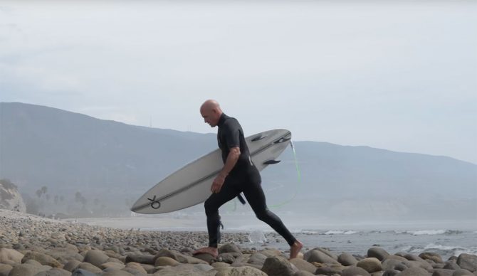 Kelly Slater walking on rocks with a surfboard