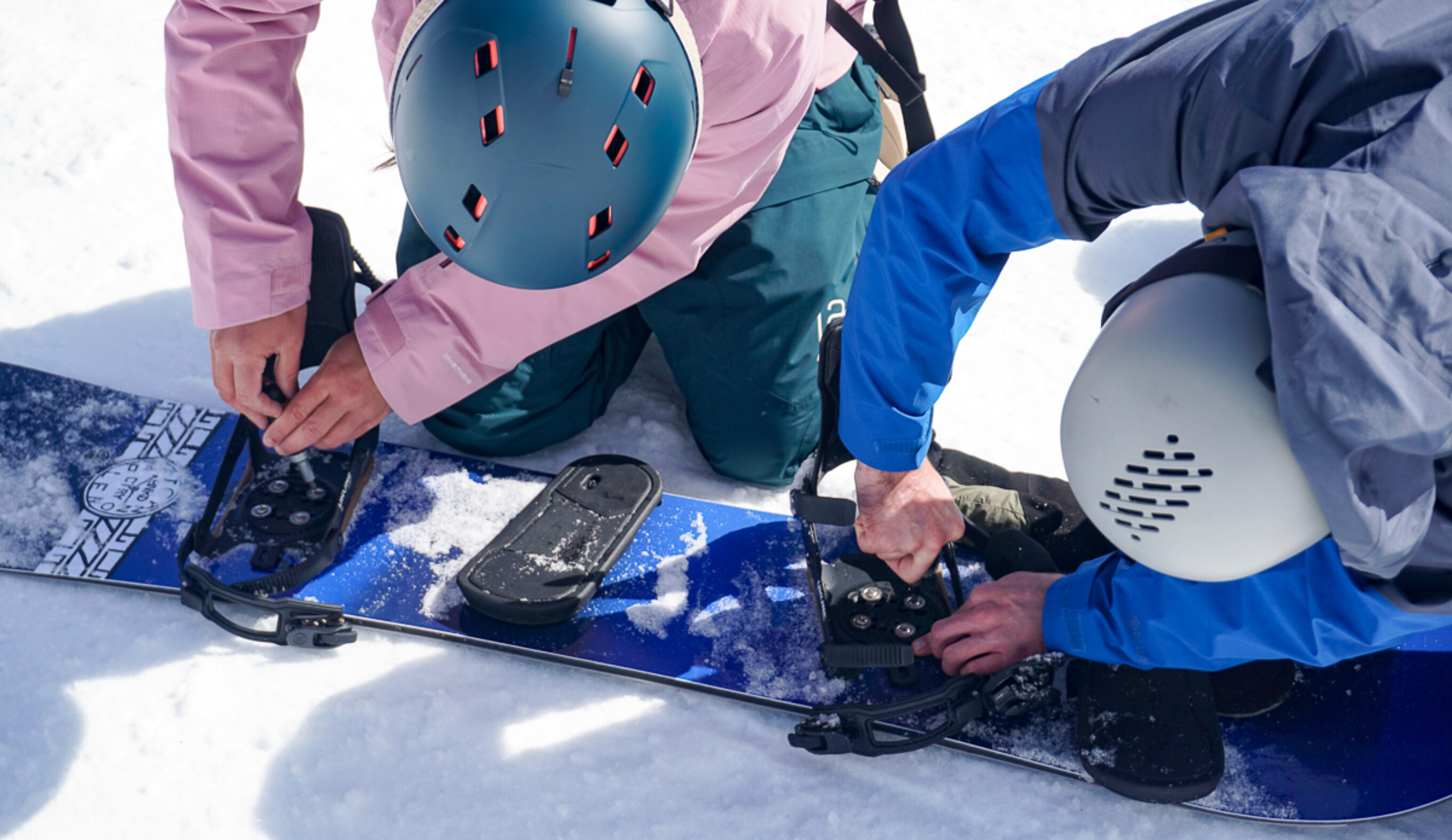 two men adjusting snowboard bindings 