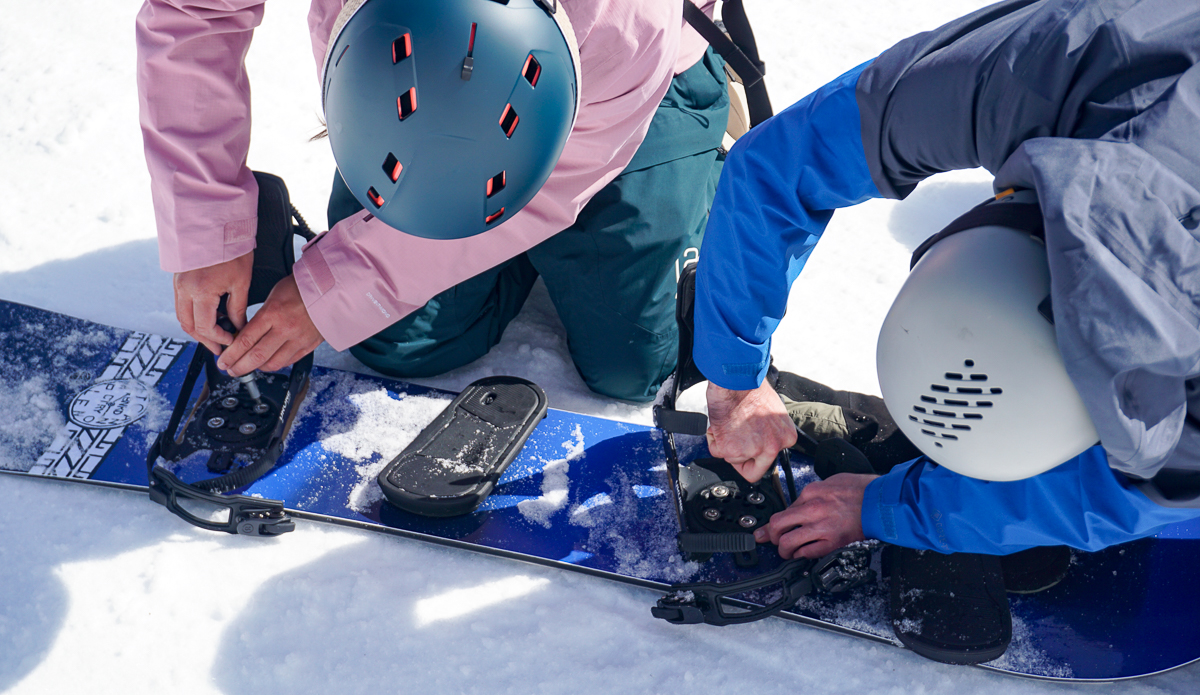 two men adjusting snowboard bindings 