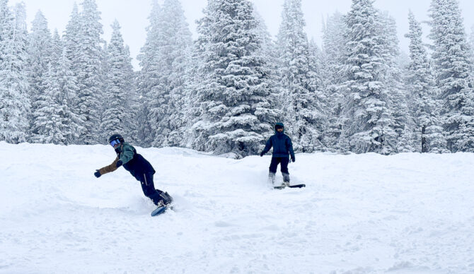 two women riding snowboards in powder