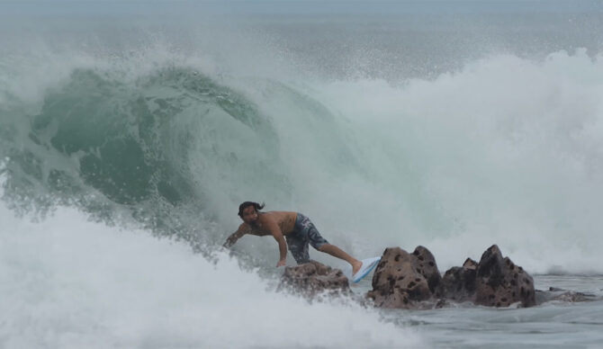 Mason Ho surfing in front of rocks