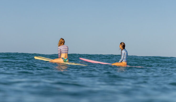 two women wearing rash guards while surfing